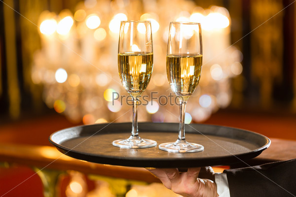 Waiter Served Champagne Glasses On A Tray In A Fine Dining Restaurant, A Large Chandelier Is In Background