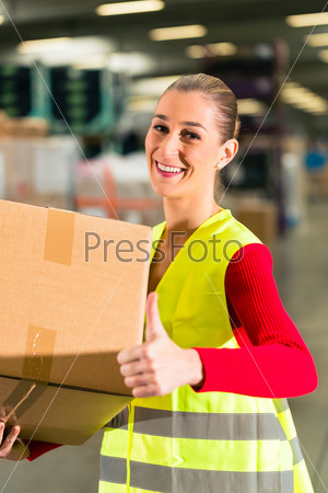 female worker with protective vest holds package, standing at warehouse of freight forwarding company
