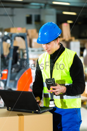 Warehouseman with protective vest, scanner and laptop in warehouse at freight forwarding company