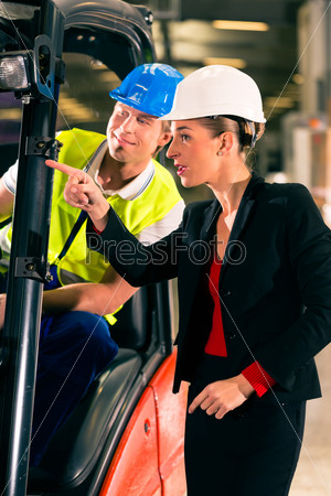 Forklift driver at warehouse of freight forwarding company, female super visor or coworker, pointing