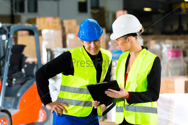 Worker or warehouseman and his coworker with clipboard at warehouse of freight forwarding company, pointing