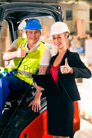 Forklift driver and female super visor with clipboard at warehouse of freight forwarding company - thumbs up