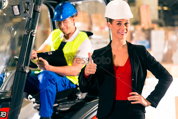 Forklift driver and female super visor with clipboard at warehouse of freight forwarding company - thumbs up