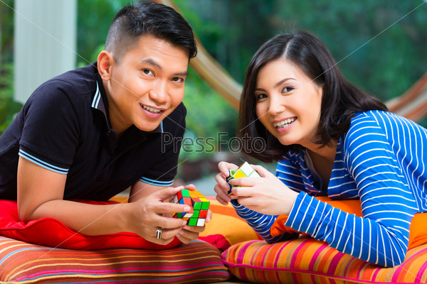 Young Indonesian couple - man and woman - at home playing with a magic cube