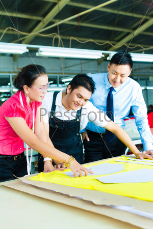 Female Designer or a seamstress, sewer, worker or production manager and owner or CEO look at pattern on a table in a textile factory