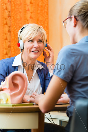 Older woman or female pensioner with a hearing problem make a hearing test and may need a hearing aid, in the foreground is a model of a human ear