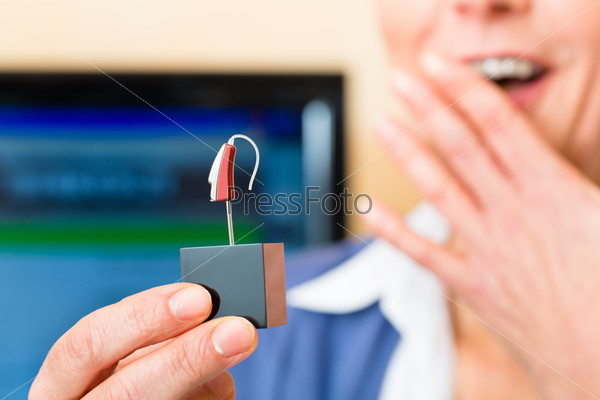 Older woman or female pensioner with a hearing problem make a hearing test, she holding a model of a hearing aid