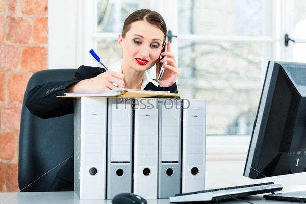 Young businesswoman working in her Office, she sits behind folders and on the telephone is a customer or client