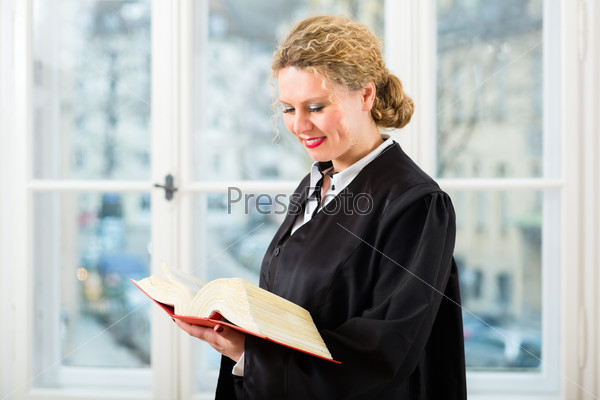 Young female lawyer working in her office reading in a typical law book, stock photo