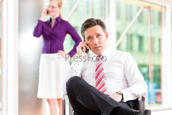 Business people - boss and secretary in office, he is sitting and she makes a phone call, stock photo