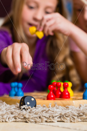 Family - two sisters - playing board game ludo at home on the floor, focus on dice in the front