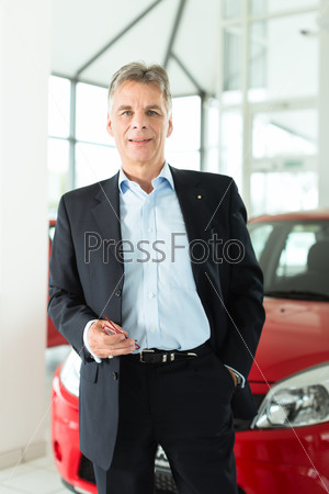 Mature single man with red auto in light car dealership, he is obviously buying a car or is a car dealer