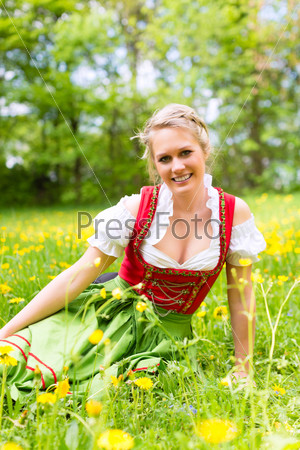 Young woman in traditional Bavarian clothes - dirndl or tracht - on a meadow in spring