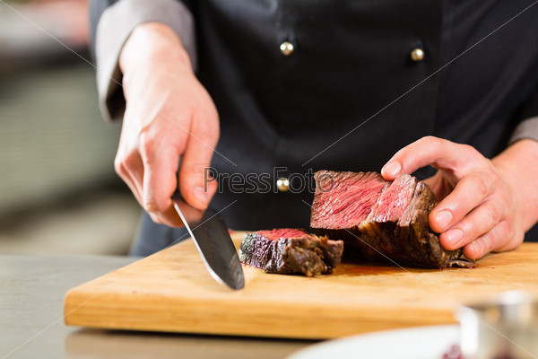 Chef in hotel or restaurant kitchen cooking, only hands, he is cutting meat or steak
