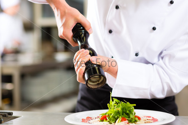 Chef in hotel or restaurant kitchen cooking, only hands to be seen, he is seasoning dishes