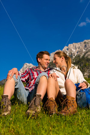 Happy Couple hiking taking a break sitting in alp meadow with mountain panorama