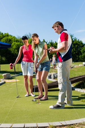 People, man and women, playing miniature golf on a beautiful summer day, stock photo
