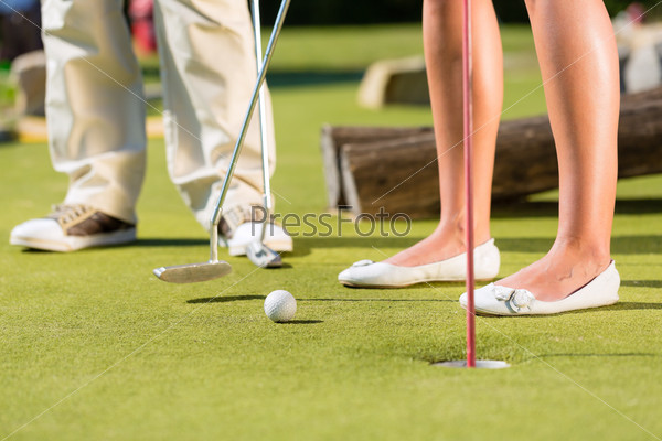 People, man and woman, only feet, playing miniature golf on a beautiful summer day