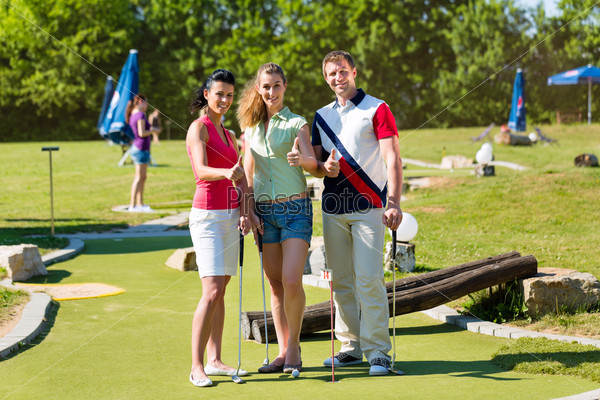 Мужчины и женщины играют в мини-гольф в прекрасный летний день