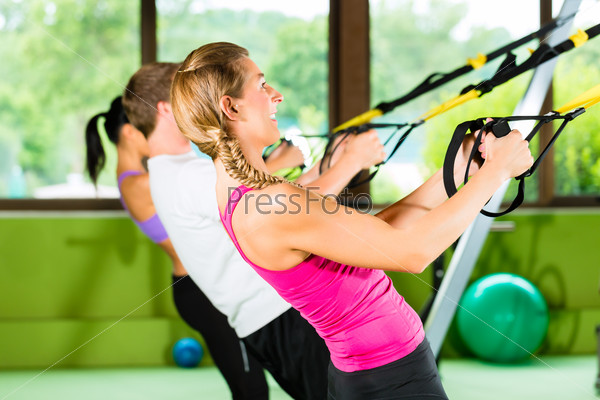 Group of people exercising with suspension trainer in fitness club or gym