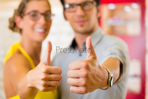 Young couple at optician in the store, they looking for glasses, thumps up