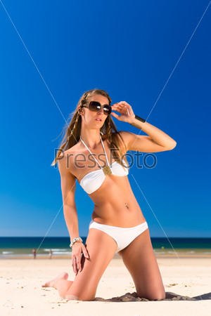 Attractive Woman in white bikini sitting in the sun on beach, a lot of copyspace in the blue sky