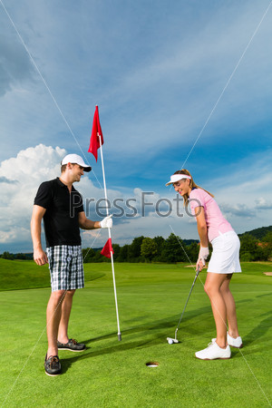 Young sportive couple playing golf on a golf course, she is putting at the green