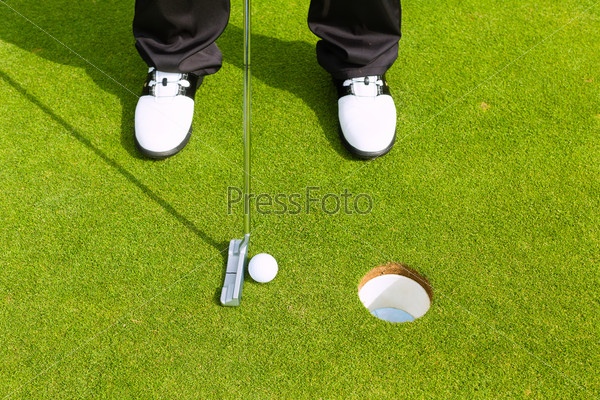 Golf player putting ball into hole, only feet and iron to be\
seen