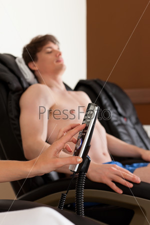 Young couple is recovering on massage chair in gym after exercising for their fitness, the woman is holding the remote control for the chair