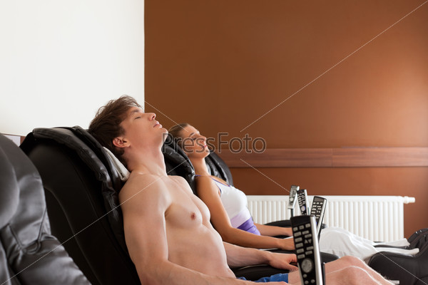 Young couple is recovering on massage chair in gym after exercising for their fitness, stock photo