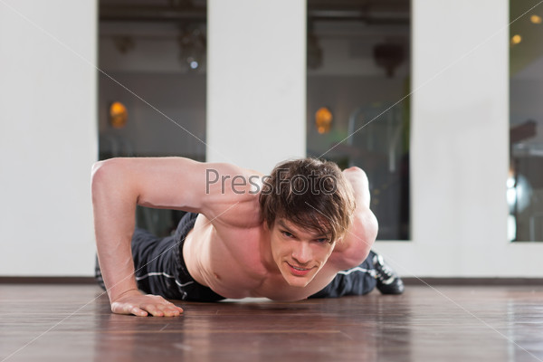 Muscular man exercising by doing pushups with only one arm in a gym