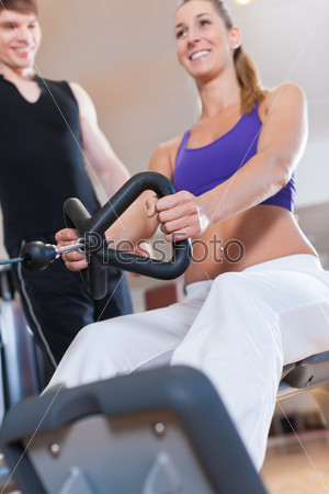 Young couple exercising in gym on different power machines to\
strengthen the muscles; the man is personal trainer