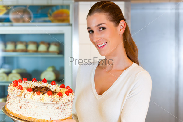 Female baker or pastry chef with torte in bakery