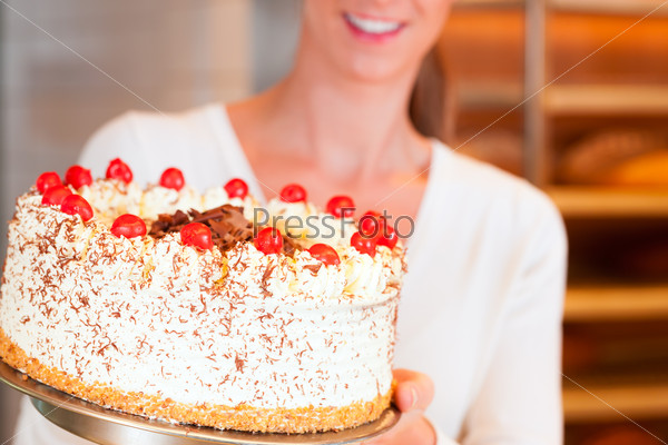 Female baker or pastry chef with torte in bakery, stock photo