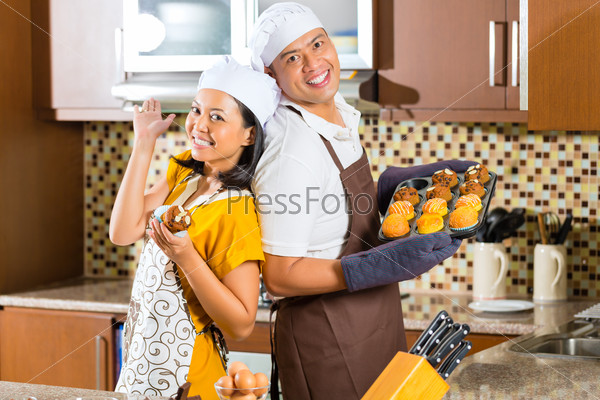 Asian couple, man and woman, presenting homemade cup cake muffins they bake in their kitchen for dessert