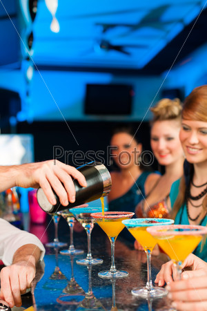 Young people in club or bar drinking cocktails and having fun; the barkeeper is mixing drinks, stock photo