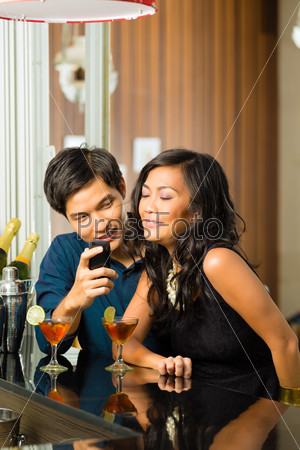 Asian man is flirting with woman in a bar having drinks, woman is shy