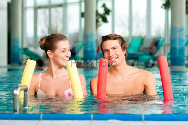 Fitness - a young couple man and woman doing sports and gymnastics or water aerobics under water in swimming pool or spa with dumbbells