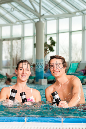 Fitness - a young couple - man and woman - doing sports and gymnastics or water aerobics under water in swimming pool or spa with dumbbells