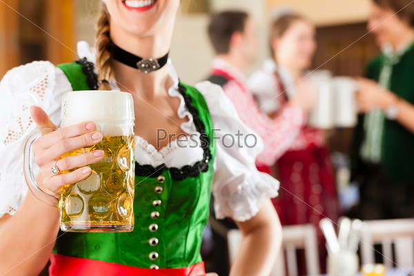 Young people in traditional Bavarian Tracht in restaurant or pub, one woman is standing with beer stein in front, the group in the background