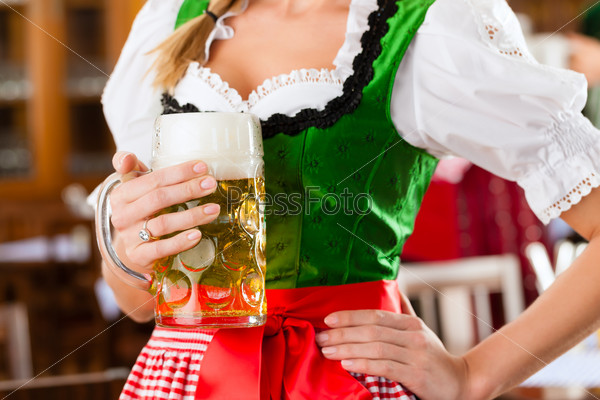 Young people in traditional Bavarian Tracht in restaurant or pub, one woman is standing with beer stein in front, the group in the background, stock photo