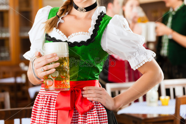 Young people in traditional Bavarian Tracht in restaurant or pub, one woman is standing with beer stein in front, the group in the background