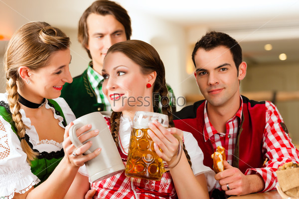 Young people in traditional Bavarian Tracht in restaurant or pub with beer and steins