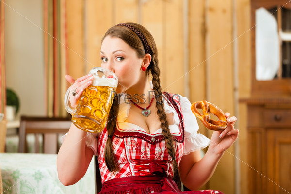 Молодая женщина в традиционном баварском костюме в ресторане или пабе с пивом и кренделем
