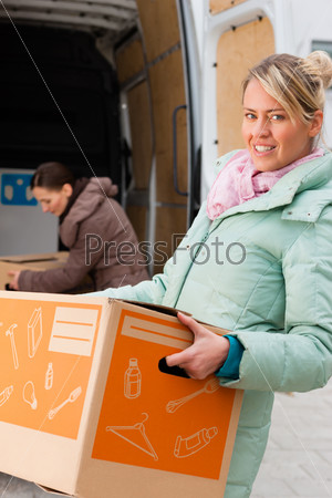Two young women loading into a moving truck, they carry moving boxes