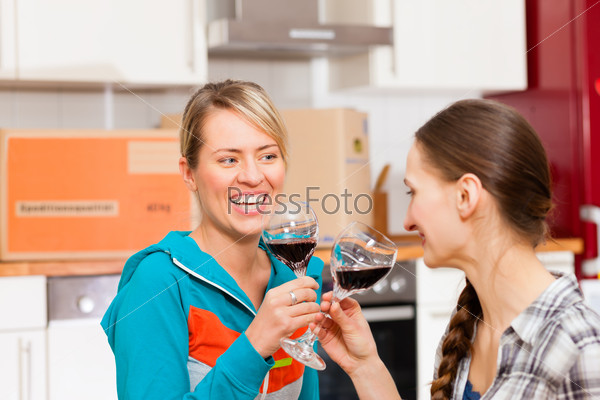 Two happy female friends moving in an apartment, they are drinking wine