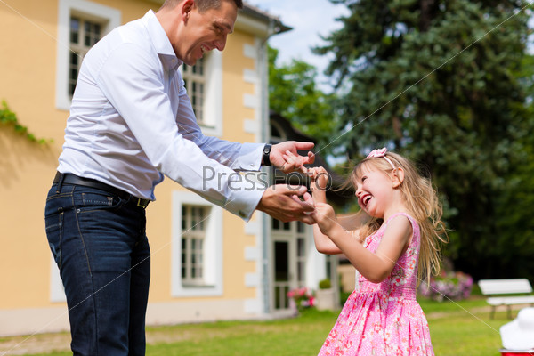 Family affairs - father and daughter playing in summer; he is dancing with her in the garden in front of the house
