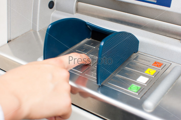 Woman at ATM or cash dispenser and is entering her PIN; only hand to be seen, stock photo