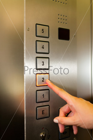 Woman in elevator or lift is pressing the button to get into the right floor; only hand to be seen - close-up