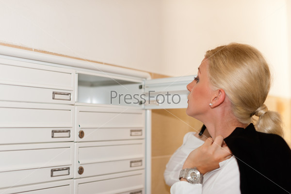 Woman is standing in front of her letter box and is looking after her mail